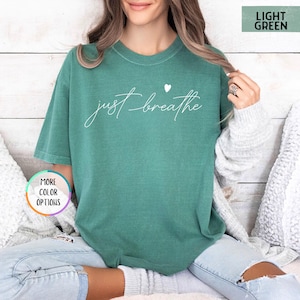 May include: A light green t-shirt with the text "just breathe" in white lettering and a small white heart above the text.