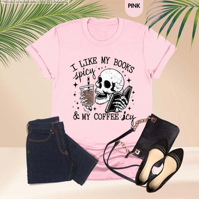 May include: Pink t-shirt with a black and white illustration of a skull holding a book and a cup of coffee. The text on the shirt reads "I like my books spicy & my coffee icy".