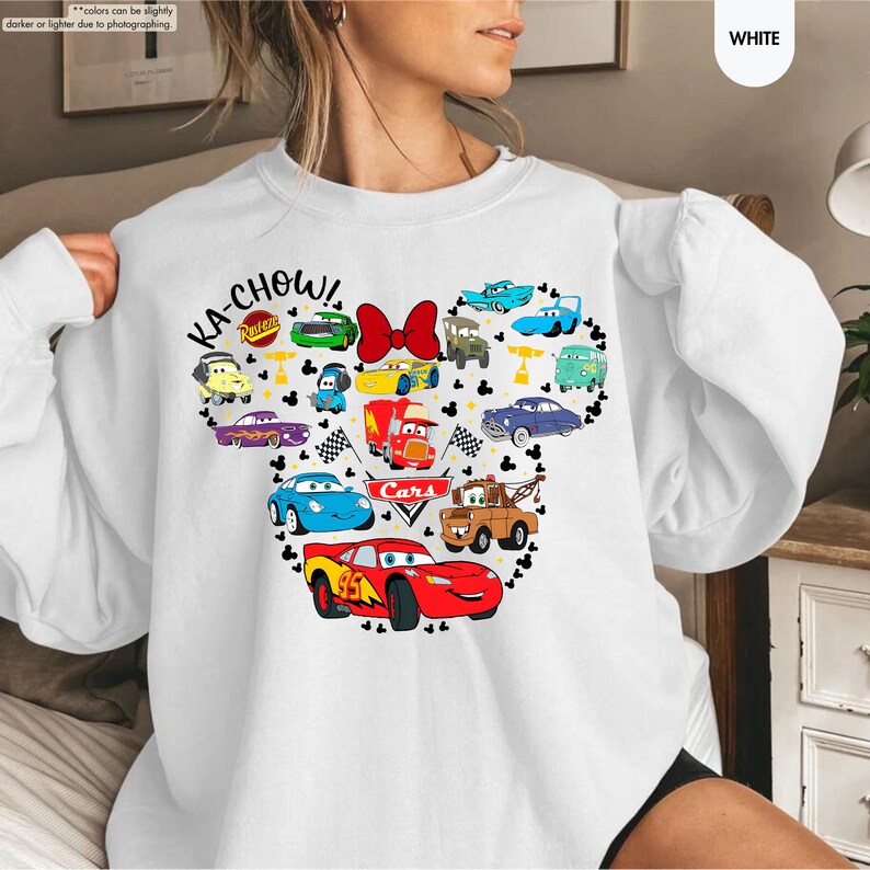 May include: White sweatshirt featuring a graphic of a Mickey Mouse head made up of Cars characters. The text "KA-CHOW!" and "Cars" are included in the graphic.