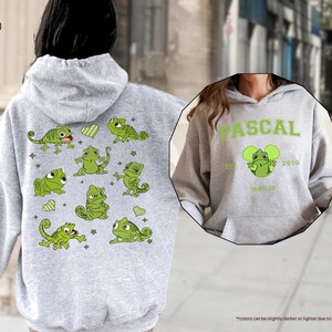 Op de afbeelding: Sportgrijze hoodie met een groen cartoonkameleonontwerp op de rug en een borstafbeelding. Het rugontwerp bevat meerdere kameleons, harten en sterren. De afbeelding op de voorkant zegt "PASCAL" boven een kameleonafbeelding en "TANGLED".
