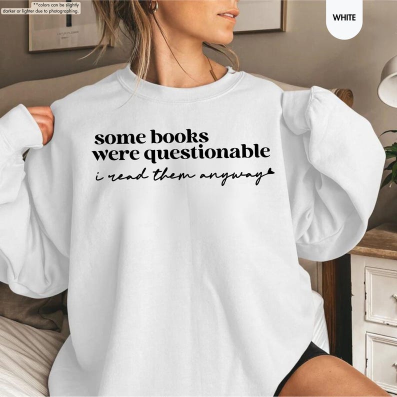 May include: A white crewneck sweatshirt featuring black text on the chest that reads some books were questionable i read them anyway. The garment has long sleeves with ribbed cuffs and a ribbed neckline, constructed from a solid white fabric.