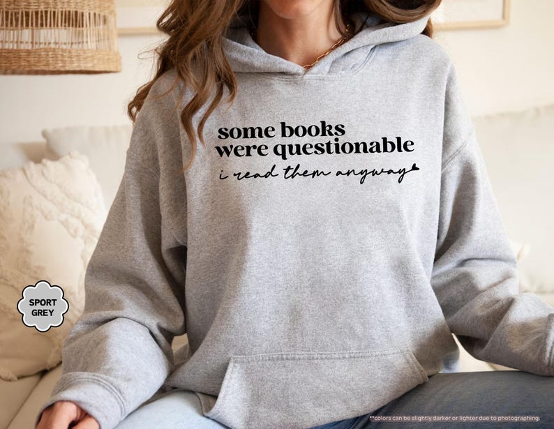 May include: A sport grey hooded sweatshirt featuring black text that reads some books were questionable i read them anyway. The garment includes a front kangaroo pocket, long sleeves, and a hood with a drawstring, crafted from a soft fabric blend.