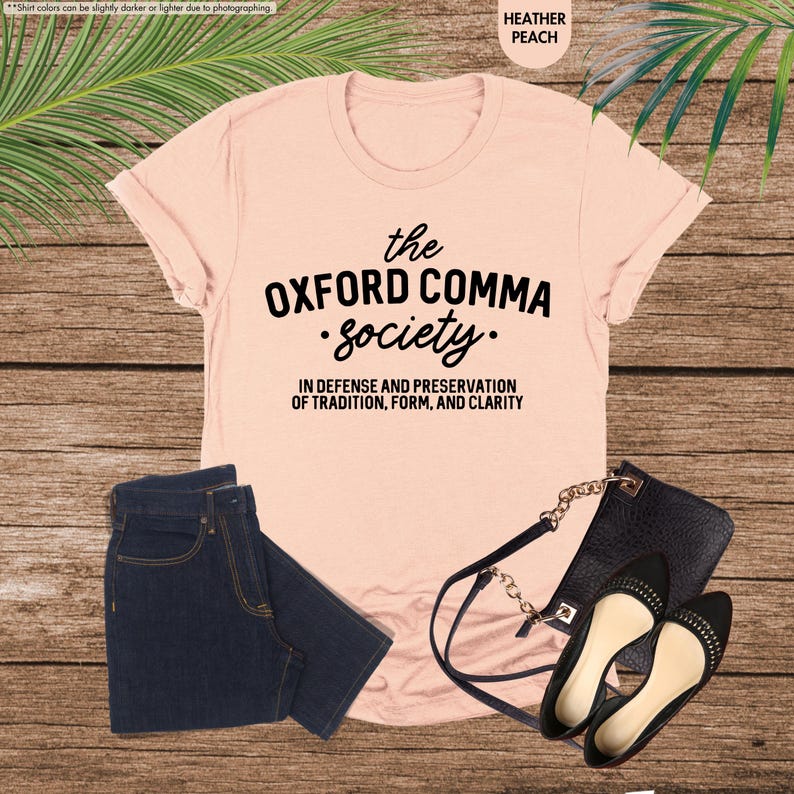 Op de afbeelding: Een roze T-shirt met de tekst "the OXFORD COMMA society." en de tekst "IN DEFENSE AND PRESERVATION OF TRADITION, FORM, AND CLARITY".