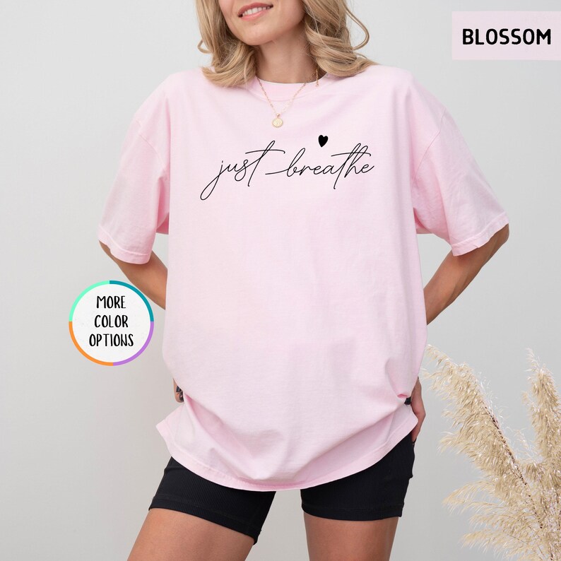 May include: A pink oversized t-shirt with the text "just breathe" in black script with a small black heart above the word "breathe".