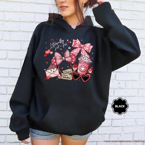 May include: Black hoodie with a graphic design featuring a pink bow, coffee cup, heart-shaped sunglasses, and the text "Literally just a girl." The design includes hearts and an envelope. The hoodie has a front pocket and a hood.