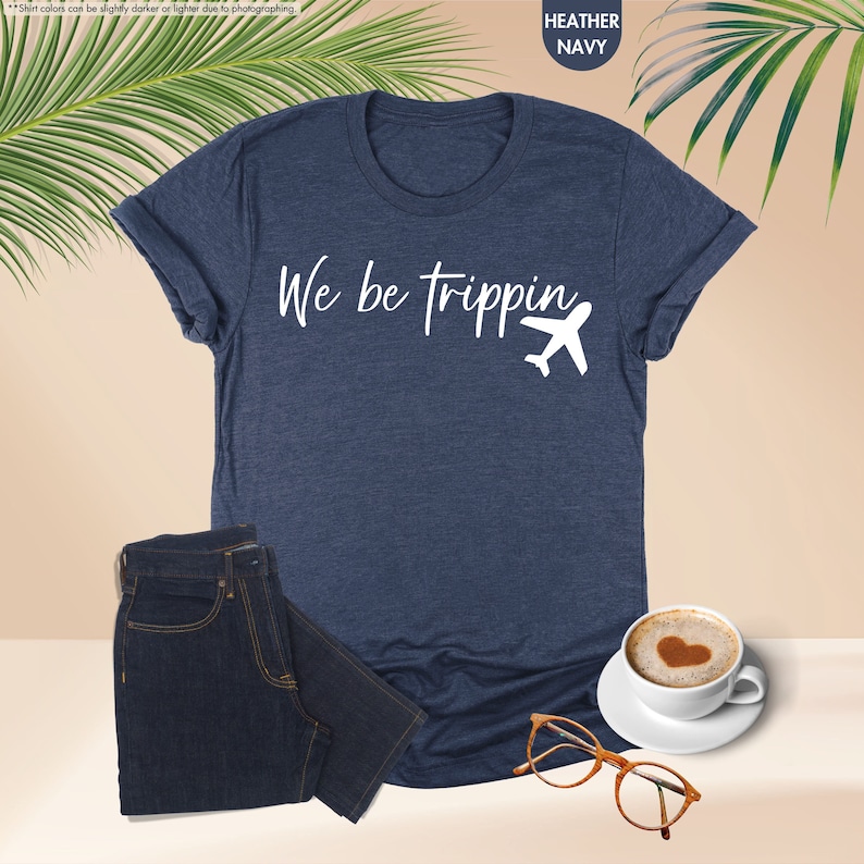 K&ouml;nnte beinhalten: Ein heidefarbenes marineblaues T-Shirt mit wei&szlig;em Text, der "We be trippin'" lautet, und einer wei&szlig;en Flugzeuggrafik.