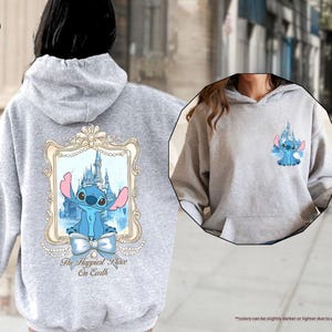 May include: A light grey hoodie featuring a cartoon image of Stitch from Lilo & Stitch. The back of the hoodie has a large framed image of Stitch in front of a castle, with the text "The Happiest Place On Earth". A smaller image of Stitch is on the front.
