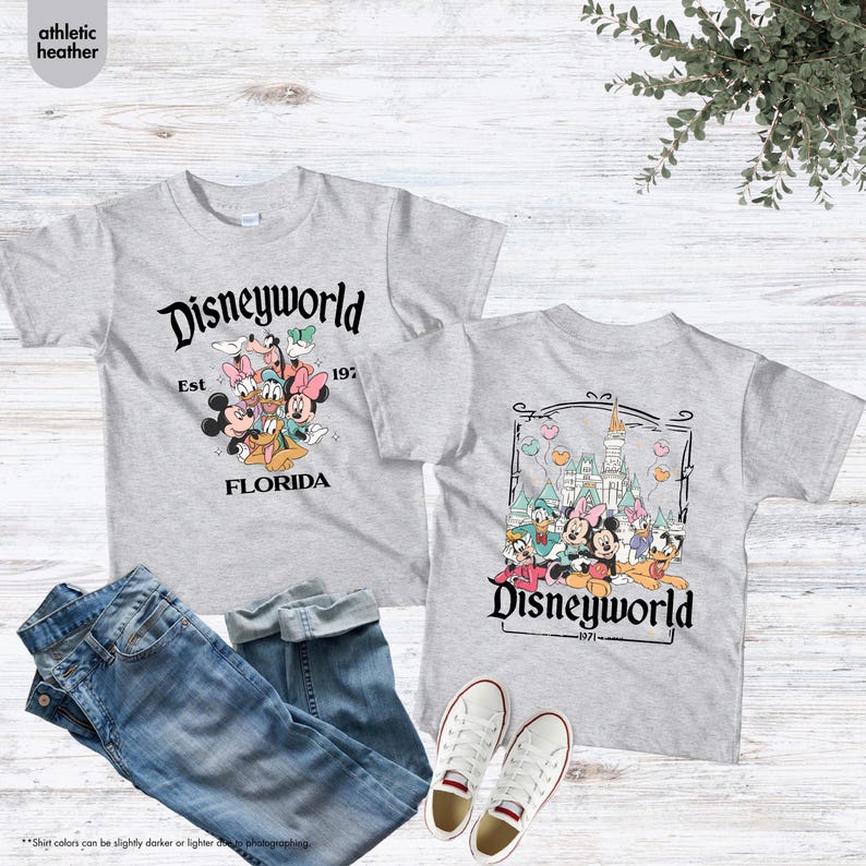 May include: Two gray t-shirts with Disneyworld graphics, jeans, and white sneakers. One shirt features Mickey, Minnie, and other characters with "Disneyworld Est 1971 Florida." The other shirt has a castle and characters with "Disneyworld 1971."
