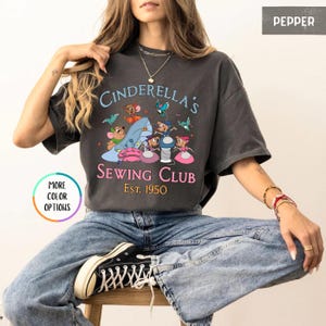 May include: A gray t-shirt with a graphic of mice sewing on a glass slipper. The text reads "Cinderella's Sewing Club Est. 1950".