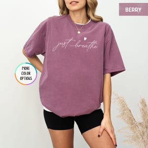 May include: A purple t-shirt with the text "just breathe" in white script with a small white heart above the word "breathe".