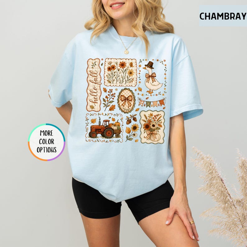 May include: A light blue t-shirt featuring a graphic print with the text hello fall, a tractor, a goose wearing a hat, floral arrangements, pumpkins, and autumn-themed patterns in brown, orange, and cream colors. The shirt has short sleeves.