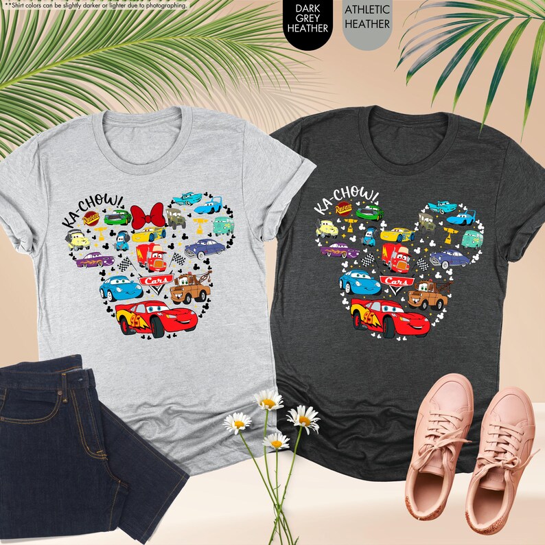 May include: Two t-shirts featuring a Mickey Mouse silhouette made up of Cars characters. The shirts are in dark grey heather and light grey heather. The text "KA-CHOW!" is printed on both shirts.