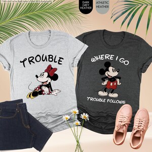 May include: Two graphic t-shirts, one light gray with Minnie Mouse and the word "Trouble", the other dark gray with Mickey Mouse and the words "Where I Go Trouble Follows". Also shown are a pair of jeans and pink sneakers.