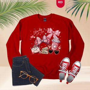 May include: A red sweatshirt with a graphic featuring a bow, hearts, and the text "Literally just a girl." The image also includes a pair of blue jeans, gold-rimmed glasses, and red trainers.