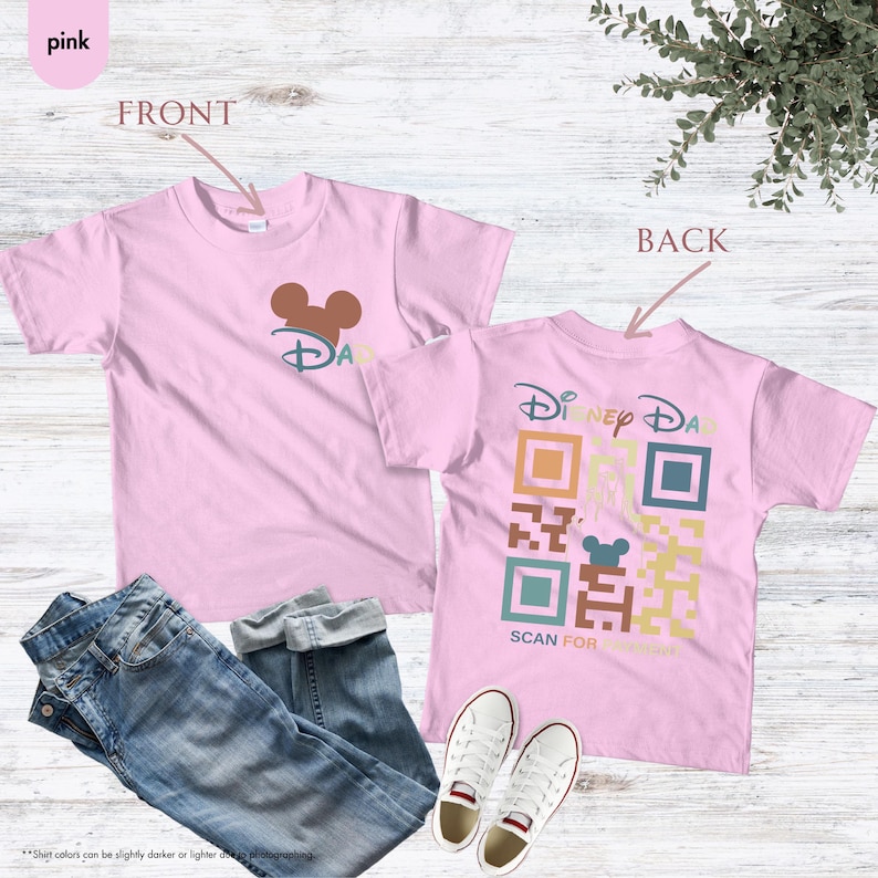 May include: Pink t-shirt with a Mickey Mouse head and the word "Disney" on the front. The back of the shirt has a colorful QR code with the text "Disney Dad" and "Scan for Surprise".