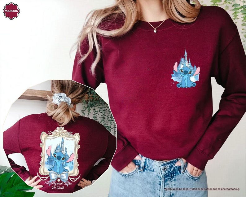 May include: Maroon sweatshirt featuring a blue cartoon character and castle design. The front has a small graphic, while the back displays a larger framed image with the text "The Happiest Place On Earth".