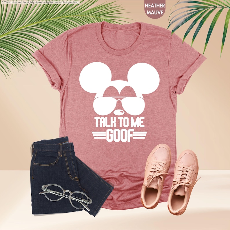 May include: Heather mauve t-shirt with a white Mickey Mouse graphic wearing sunglasses and the text "TALK TO ME GOOF". The image also includes dark blue jeans, eyeglasses, and pink trainers.