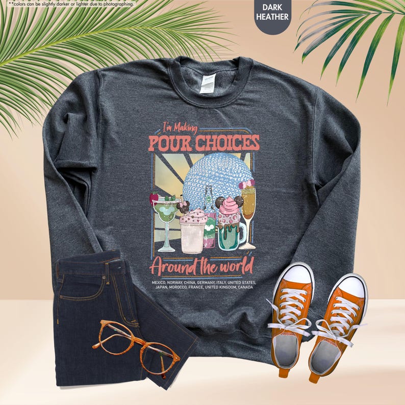 Pu&ograve; includere: Felpa grigio scuro con la scritta "I'm Making Pour Choices Around the World" e grafica di cocktail. L'immagine include un paio di jeans blu, scarpe da ginnastica arancioni e occhiali.