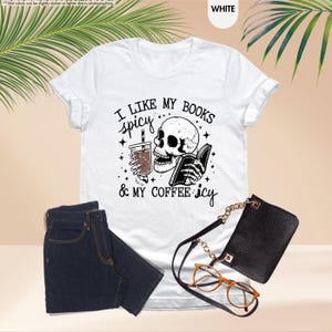 May include: White t-shirt with a black and white illustration of a skeleton holding a book and a cup of coffee. The text on the shirt reads "I like my books spicy & my coffee icy".