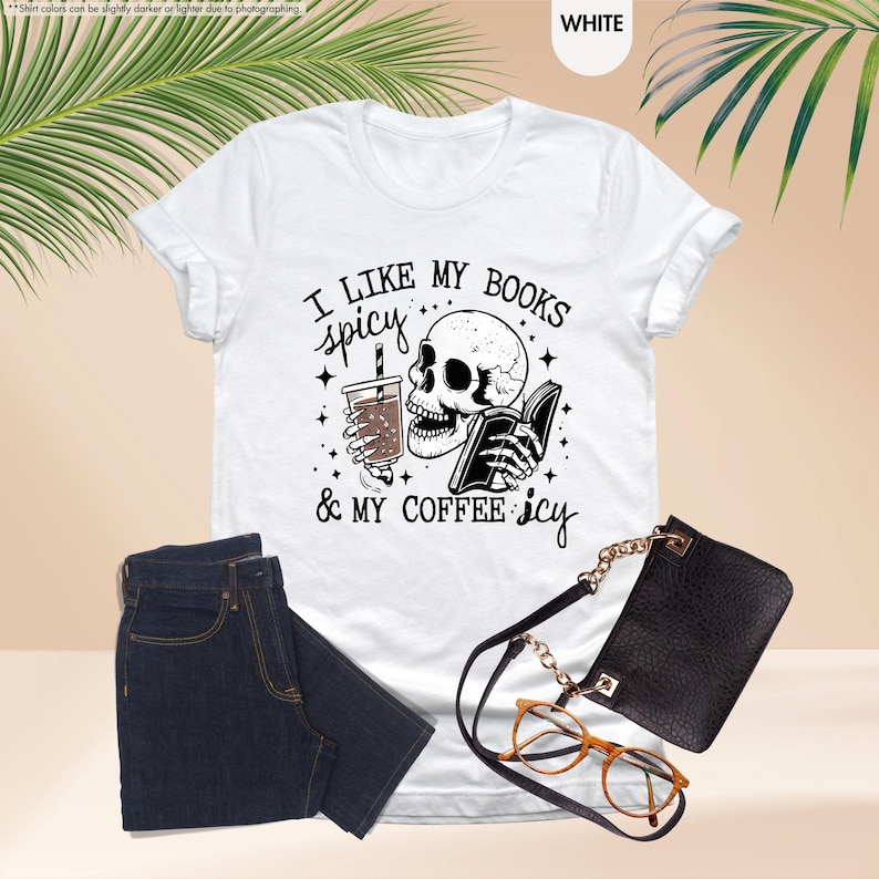 May include: White t-shirt with a black and white illustration of a skeleton holding a book and a cup of coffee. The text on the shirt reads "I like my books spicy & my coffee icy".