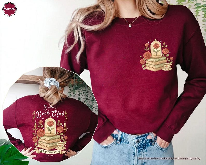 Puede incluir: Sudadera granate con un dise&ntilde;o floral que incluye una rosa, libros y una taza de t&eacute;. La parte delantera tiene un peque&ntilde;o gr&aacute;fico, mientras que la parte trasera muestra "Belle's Book Club" con el texto "Tale as Old as Time".