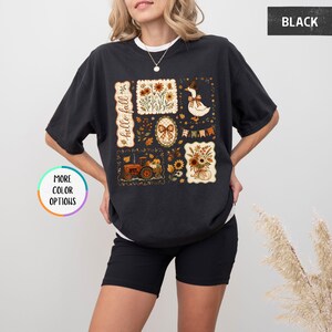 May include: A black short-sleeve t-shirt featuring a graphic print with the text hello fall. The design includes illustrations of a goose, a tractor, sunflowers, autumn leaves, a bow, and bunting flags arranged in a rectangular grid pattern.