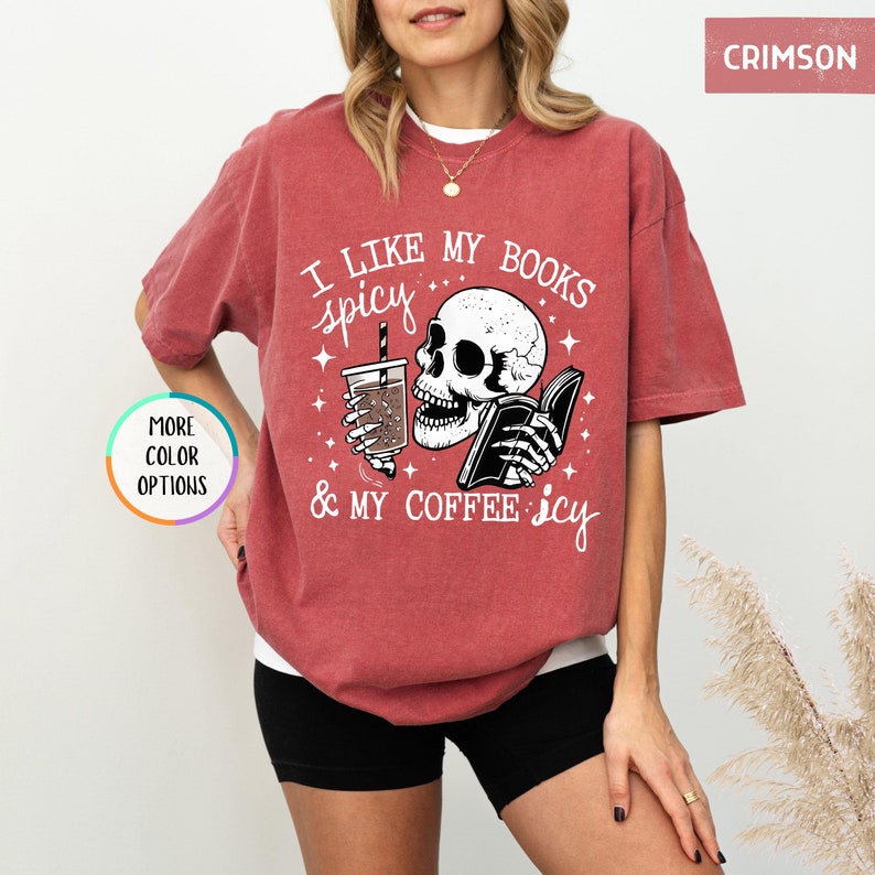 May include: Crimson t-shirt featuring the text "I like my books spicy & my coffee icy" and a skull graphic reading a book and holding a coffee. The shirt has a loose fit.