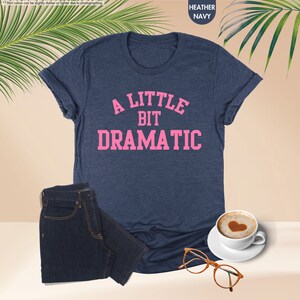 a t - shirt that says a little bit dramatic next to a cup of coffee