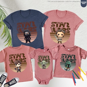 May include: Set of four Star Wars themed t-shirts in heather navy and heather mauve. The shirts feature a retro-style graphic with the text "Star Wars" and a cartoon character from the Star Wars franchise. The characters are Kylo Ren, Rey, Han Solo, and Boba Fett.