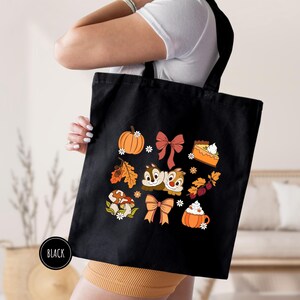 a woman holding a black bag with a bunch of cats and pumpkins on it