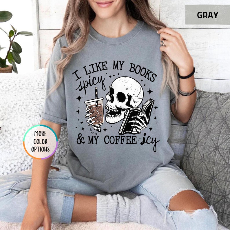 May include: Grey t-shirt featuring a skull graphic with a drink and book. The text says "I LIKE MY BOOKS spicy & MY COFFEE icy". The shirt has a crew neck and short sleeves.
