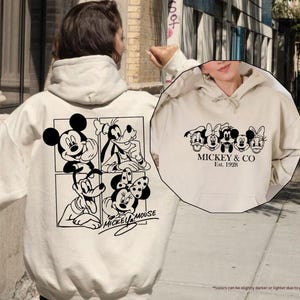 May include: Sand-colored hoodie featuring Mickey Mouse and friends in black and white graphics. The back displays Mickey, Goofy, and Minnie Mouse, while the front showcases the text "Mickey & Co. Est. 1928".
