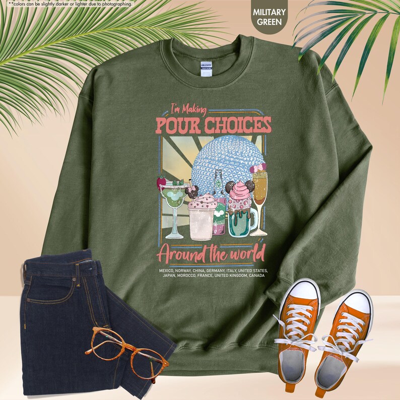 Pu&ograve; includere: Felpa verde militare con la scritta "I'm Making Pour Choices Around the World" e una grafica di cocktail e una sfera blu. La felpa &egrave; abbinata a jeans blu scuro e scarpe da ginnastica arancioni.