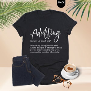 a t - shirt with the words adulting on it next to a cup of