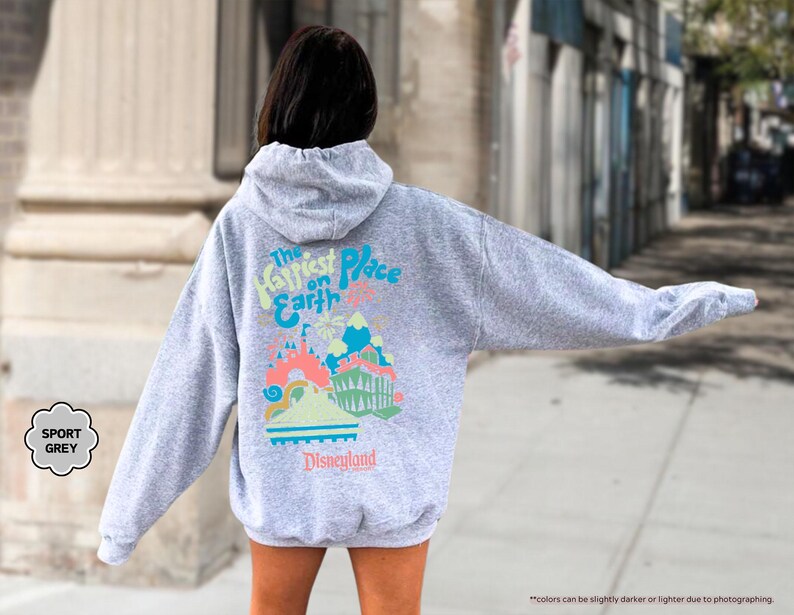 Pu&ograve; includere: Una felpa con cappuccio grigia con il testo "The Happiest Place on Earth" e una grafica del castello di Disneyland. Il testo "Disneyland" &egrave; sotto la grafica.