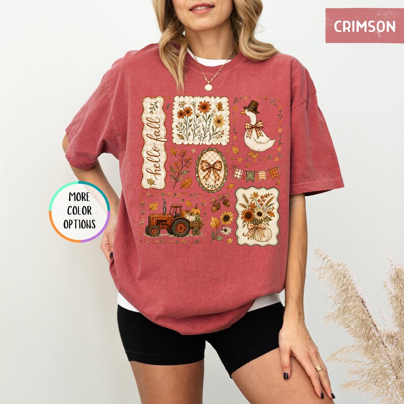 May include: A crimson short-sleeve t-shirt featuring a graphic print with the text hello fall. The design includes a goose wearing a hat, a tractor, sunflowers, pumpkins, and autumn leaves arranged in rectangular and oval frames on the front.