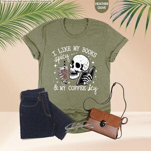 May include: Green t-shirt with a white graphic of a skull holding a book and a coffee cup. The text on the shirt reads "I like my books spicy & my coffee icy".
