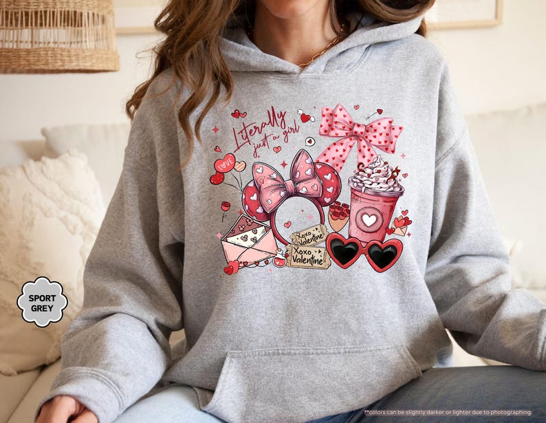 May include: A light grey hoodie featuring a Valentine's Day design. The design includes a pink bow, heart-shaped sunglasses, a coffee cup, and the text "Literally just a girl." The hoodie is labeled "Sport Grey."