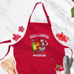 May include: Red apron with the words "GRILL MASTER" and a cartoon character grilling. The name "ANDREW" is printed below the character. The apron has a pocket and adjustable neck strap.
