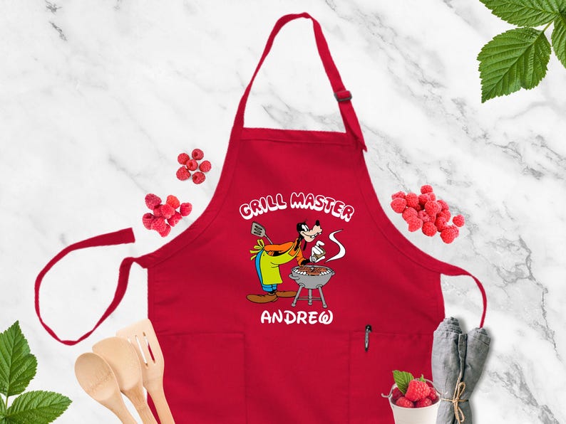 May include: Red apron with the words "GRILL MASTER" and a cartoon character grilling. The name "ANDREW" is printed below the character. The apron has a pocket and adjustable neck strap.