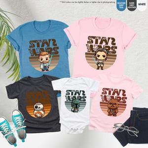 May include: A set of four t-shirts featuring Star Wars characters in a retro style. The shirts are in various colors, including blue, pink, white, and grey. Each shirt has a different character, including Obi-Wan Kenobi, Rey, Boba Fett, and R2-D2. The shirts all have the text "Star Wars" in a vintage font.