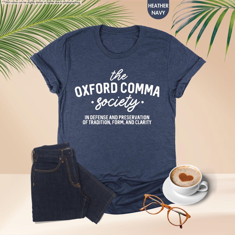 Op de afbeelding: Een marineblauw t-shirt met de tekst "the OXFORD COMMA Society." en de tekst "IN DEFENSE AND PRESERVATION OF TRADITION, FORM, AND CLARITY".