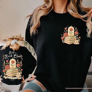 Puede incluir: Sudadera negra con un dise&ntilde;o de una rosa en una c&uacute;pula de cristal sobre libros, rodeada de rosas y una taza de t&eacute;. La parte trasera de la sudadera tiene el texto "Belle's Book Club" y "Tale as Old as Time".