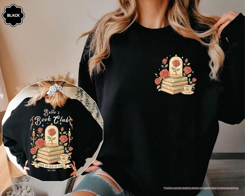 Puede incluir: Sudadera negra con un dise&ntilde;o de una rosa en una c&uacute;pula de cristal sobre libros, rodeada de rosas y una taza de t&eacute;. La parte trasera de la sudadera tiene el texto "Belle's Book Club" y "Tale as Old as Time".