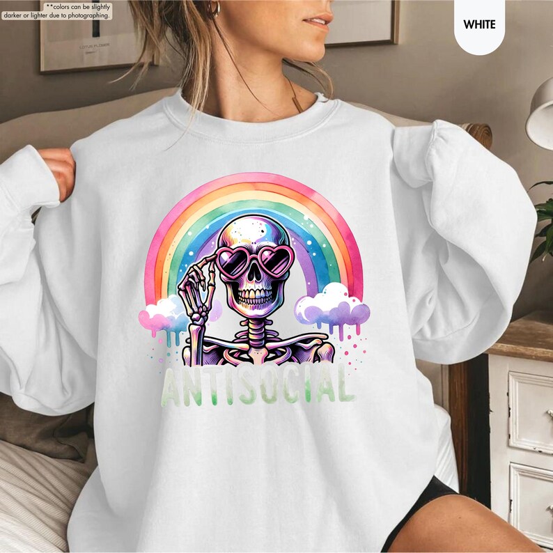 May include: White sweatshirt with a skeleton wearing heart-shaped sunglasses, set against a rainbow backdrop. The word "ANTISOCIAL" is printed in green below the skeleton. The design is vibrant and colourful.