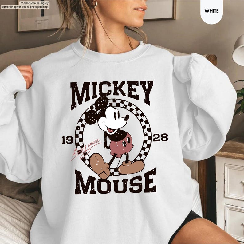 May include: White sweatshirt featuring a vintage Mickey Mouse graphic. The design includes the words "MICKEY MOUSE" and the year "1928" in a retro font. The cartoon character is in the center, with a checkered circle behind it.