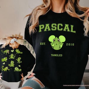 Op de afbeelding: Zwarte sweatshirt met een groene afbeelding van Pascal de kameleon uit de film Rapunzel. Het ontwerp bevat de naam "PASCAL", het jaar "2010" en het woord "TANGLED". De achterkant heeft een kleinere afbeelding van Pascal en andere kameleons.