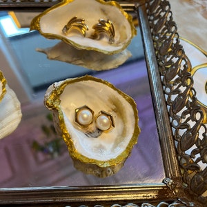 May include: Two pairs of earrings displayed in gold-painted oyster shells. One pair is gold and the other is pearl.