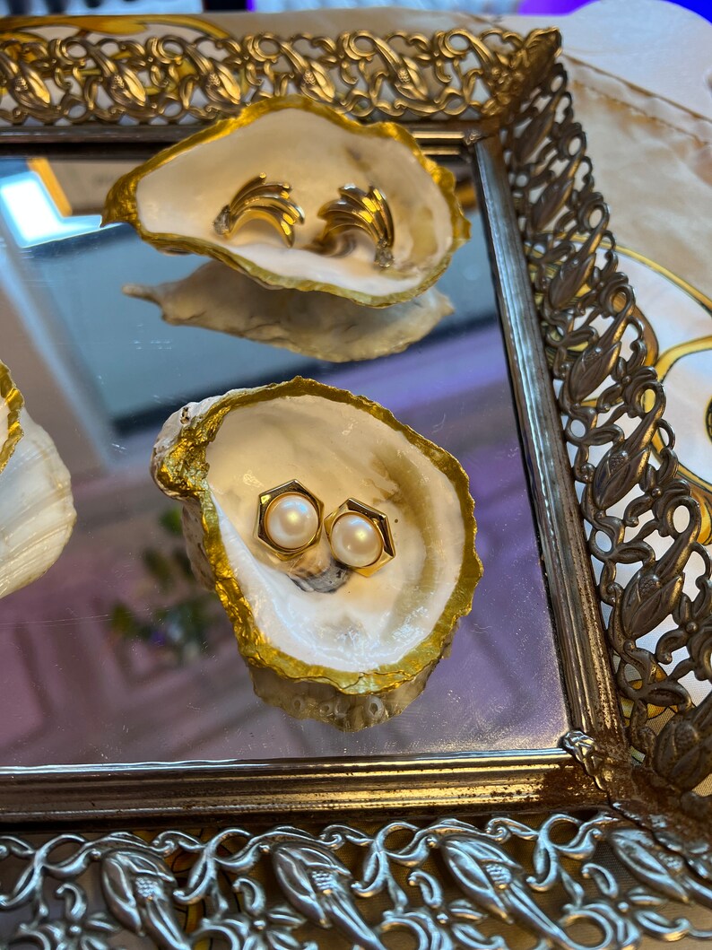 May include: Two pairs of earrings displayed in gold-painted oyster shells. One pair is gold and the other is pearl.