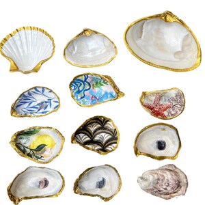 May include: Twelve seashells with gold trim, some are plain white, others are decorated with various patterns, including floral, geometric, and nautical designs.